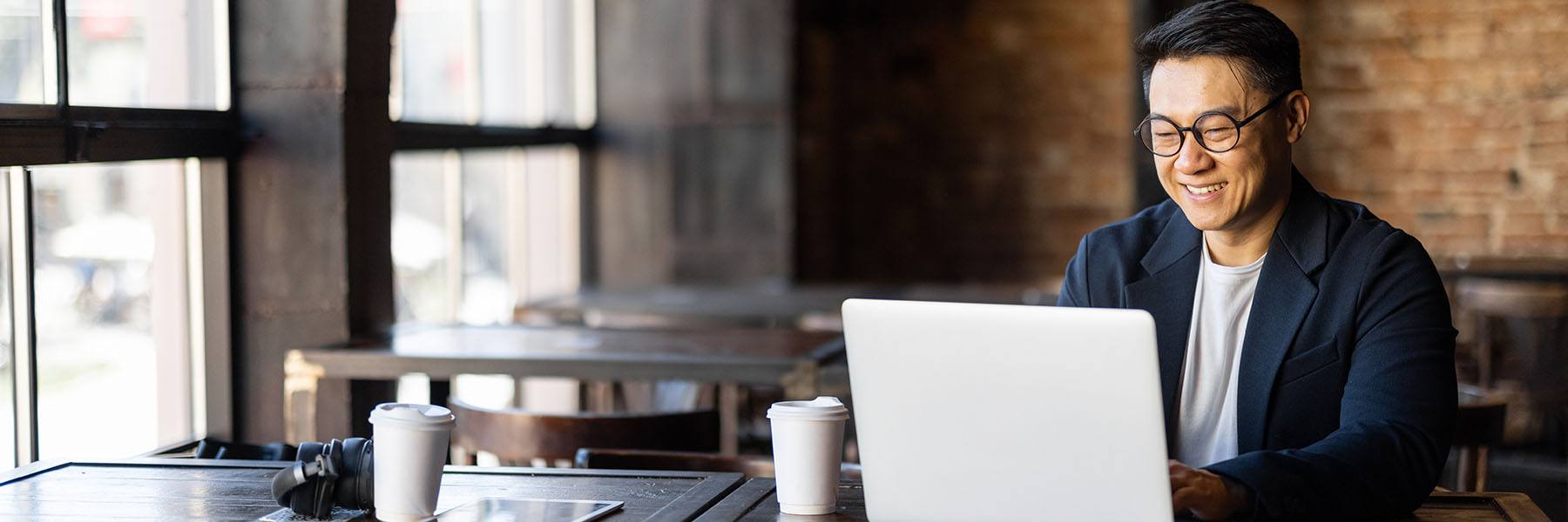 Man sits at a coffee shop table looking at his laptop
